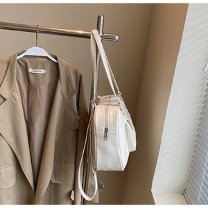 Détail d'un sac messager minimaliste en similicuir crème suspendu à un cintre en métal