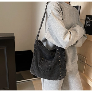Detail of dark gray washed denim tote bag featuring side metal rivets and chain strap