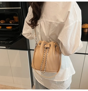 Detail of beige pleated drawstring bucket bag with metal chain strap on model