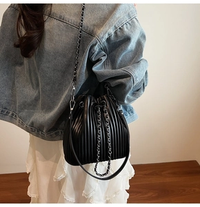 Detail of black pleated bucket bag with chain strap worn by a model in denim