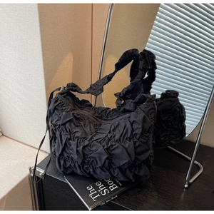 Detail shot of black pleated cloud bag with organza texture on a minimalist book stand
