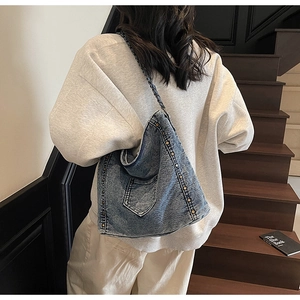 Close-up detail of blue washed denim shoulder bag featuring stylish metal rivets and chain strap