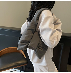 Detail of grey quilted puffy tote bag featuring a large bow design worn by a model