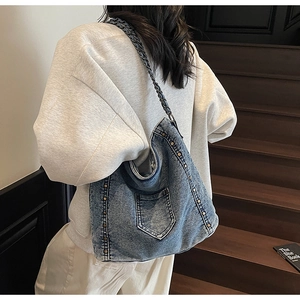 Detailed back view of a denim tote bag with rivets and chain strap on a model