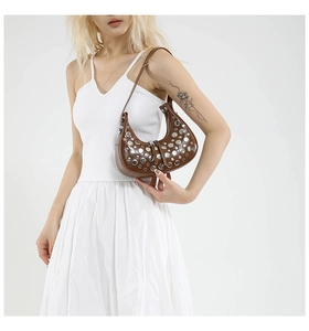 Detail of brown crescent bag with silver rivets and glossy finish on model