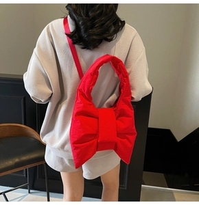 Rear view of a model wearing a bright red puffy bow crossbody bag in lightweight nylon