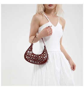 Detail of burgundy leather crescent bag with silver stud rivets worn by a model