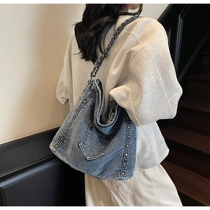 Detail of blue denim tote bag with silver studs and black metal chain on shoulder