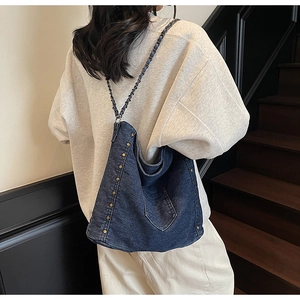 Detail of dark blue denim tote with metallic rivets and woven chain strap on stairs