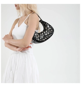 Close-up of black crescent moon bag with silver rivets shown on a model's shoulder