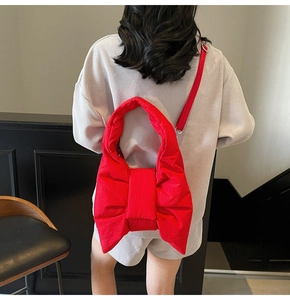Detail of red bow quilted tote bag with wide strap worn as a shoulder bag on a model