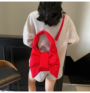 Detail view of a large red bow-shaped quilted puffer tote bag on a model's shoulder