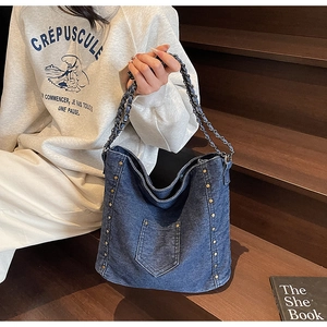 Close-up of a blue denim tote bag with gold stud rivets and chain shoulder strap detail