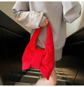 Close-up of a large red puffy bow tote bag with soft padded texture in a street style view