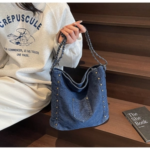 Detail of blue denim crossbody bag featuring gold studs and black leather chain strap