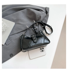 Detail der schwarzen Lackledertasche mit Nieten und Spikes neben einem Handy als Vergleich