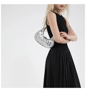 Silver metallic crescent moon bag with rivet detailing worn as a chic underarm shoulder bag