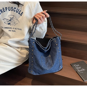Detail of vintage denim tote bag with metal rivets and chain strap on a model