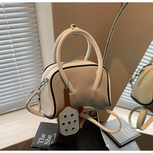Detail of white boston bag with black piping and charm decoration next to a mirror
