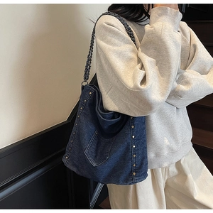Detail of dark blue denim tote bag with metal rivets and stylish chain shoulder strap