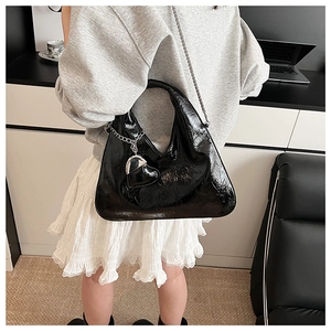 Detail of black patent leather hobo bag with heart pendant worn by a model