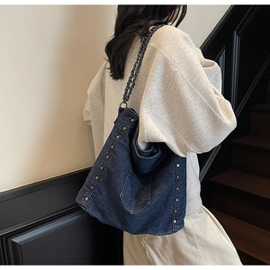 Detail of dark blue denim tote bag with metal rivets and chain strap on a model