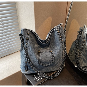 Detail of washed blue denim hobo bag with brass rivets and thick metal chain strap