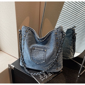 Detail of denim tote bag featuring studded edges and woven chain shoulder strap