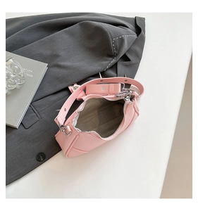 Draufsicht auf die rosa Nieten-Umhängetasche mit silbernen Details neben grauem Blazer