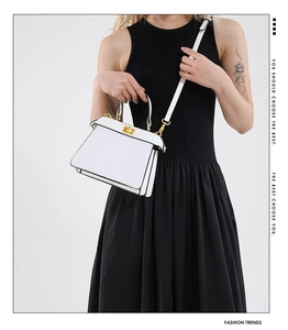 Detailed view of white crocodile texture handbag with gold metal clasp and black piping
