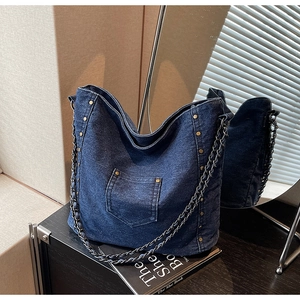 Close-up of deep blue denim tote bag with side rivets and metal chain woven strap