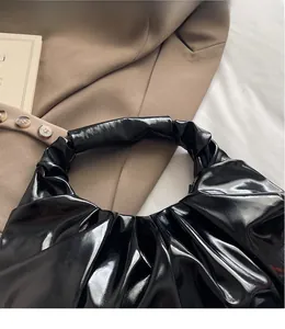 Detail of black glossy pleated handbag with premium patent leather texture and handle