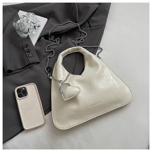 Detail of a cream triangle bag with glossy pleated texture and heart-shaped pendant charm