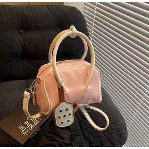 Pink macaron Boston bag with contrast white piping and stylish charm on a plush sofa