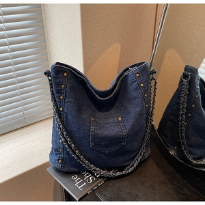 Close-up of dark blue denim hobo bag featuring metal rivets and braided chain strap details