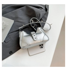 Detailansicht der silbernen Metallic-Tasche mit Nietengurt und Schnalle neben Handy