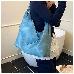 Blue faux leather tote bag and matching pouch shown on a shoulder in a modern room