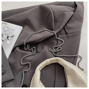 Detail of off-white patent leather handbag with silver metal chain on dark grey suit