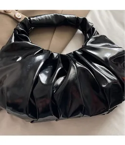 Detailed view of black patent leather hobo bag featuring handcrafted vertical pleats