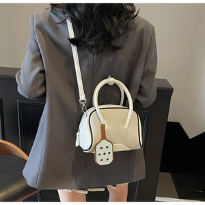 Detail of a minimalist white bowling handbag showing leather texture and logo tag decor