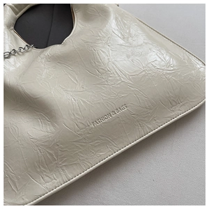Macro detail of creamy white pleated texture and metal chain on modern handbag