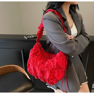 Close-up of bright red cloud bag with pleated texture worn by a model in a modern room