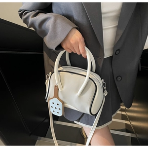 Detail of cream white bowling bag with racquet charm on a gray outfit lifestyle model