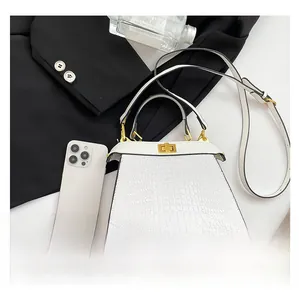 Detailed view of white crocodile pattern leather handbag with gold twist lock and shoulder strap