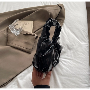 Detail of a black glossy pleated handbag featuring a ruched top handle and chic finish