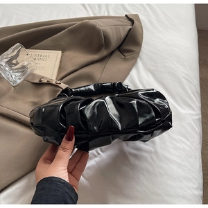 Detail of black glossy pleated handbag next to a blazer and glass on a bed