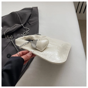 Detail of cream pleated handbag with heart charm and silver chain strap on grey fabric