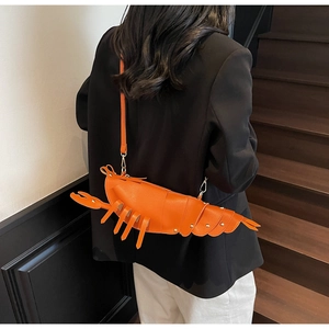 Detail of creative orange lobster-shaped crossbody bag with gold rivet accents on strap