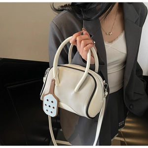Detail of cream Boston handbag featuring black piping and a mini racket pendant