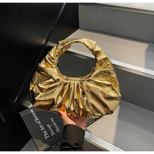 Detail of gold ruched hobo bag with metallic finish and crescent shape in hand